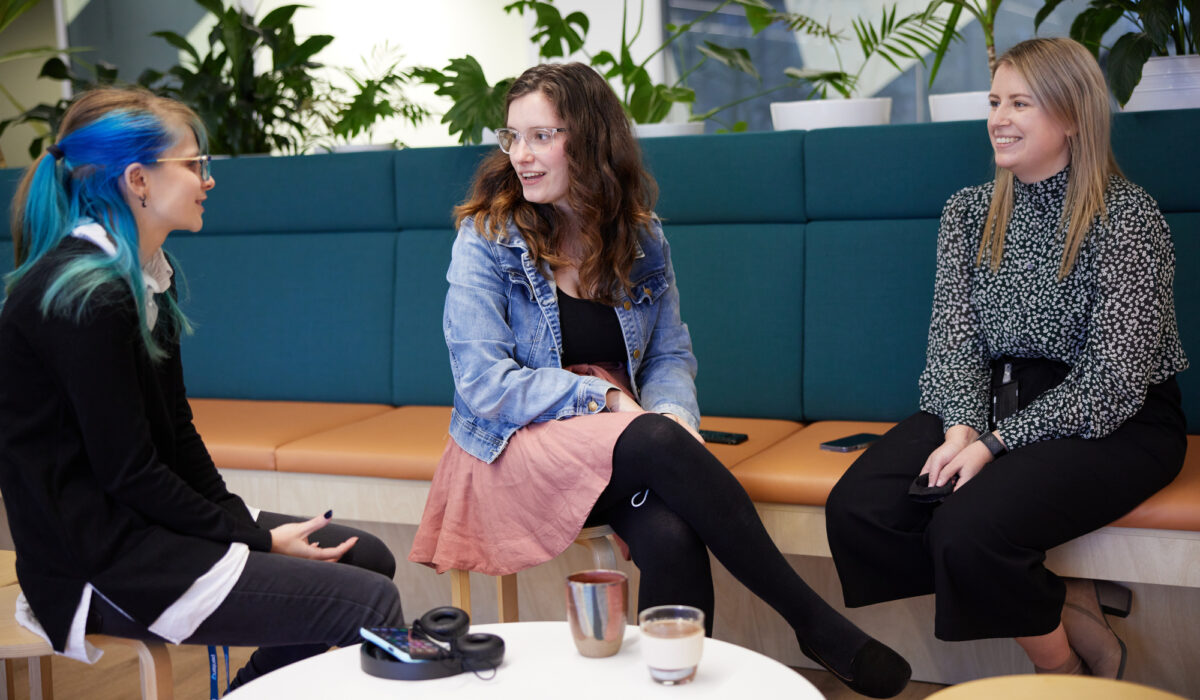 A trio of female employees sitting on some casual seating while chatting